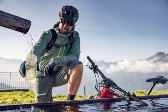 Radfahrer füllt Trinkflasche bei Brunnen auf, Zillertal