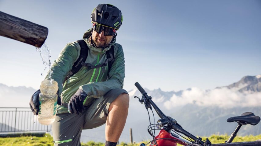 Radfahrer füllt Trinkflasche bei Brunnen auf, Zillertal
