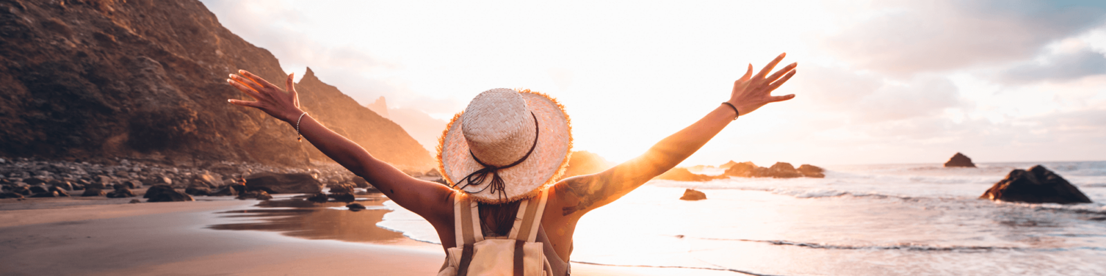Urlaub am Meer Eine Frau steht am Strand mit ausgestreckten Armen und sieht aufs Meer hinaus.